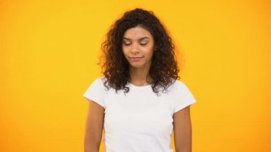 Biracial kız fısıldayan sırları gülümseyen ve kamera sarı arka plan göz kırpıyor