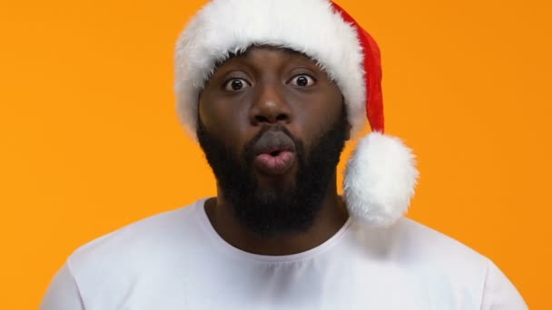 黄色の背景をクリスマス帽子でアフリカ系アメリカ人の男を驚かせた発表 — ストック動画