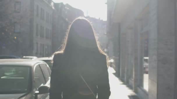 Succesvolle vrouw langzaam lopend onderaan de straat, heldere zon balken verlichten van haar — Stockvideo