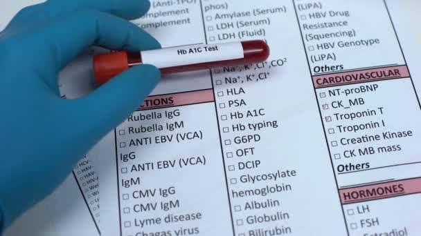 Тест на Hb A1C, врач проверяет имя в лабораторном бланке, показывая образец крови в пробирке — стоковое видео