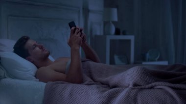 Uykulu erkek yatakta yatarken ve sabah uyanmak için alarm ayarı cep telefonu kullanarak