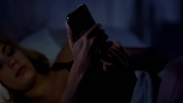 女性がベッドに横たわっていると スマート フォンでチャット オンライン ショッピング ガジェット中毒 — ストック写真