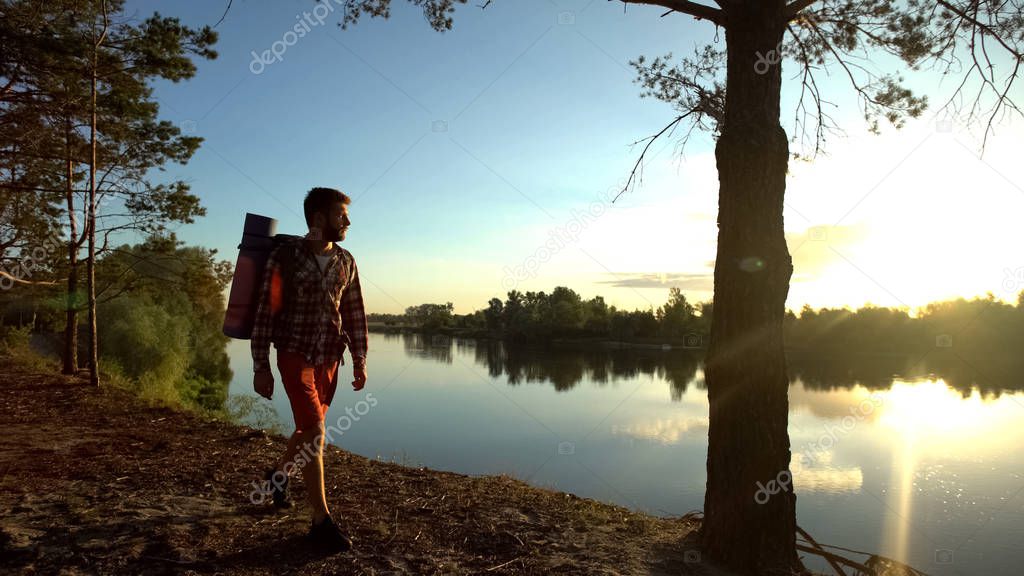 Hiker walking along river bank in magnificent place, enjoying beautiful view