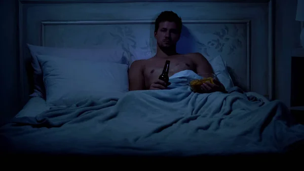 单身男性躺在床上 看电视秀和吃零食 懒散的周末 — 图库照片