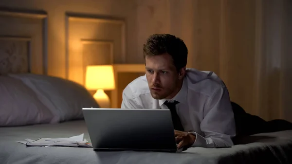 Серьезный Человек Лежит Кровати Улучшает Бизнес Знания Интернете Помощью Ноутбука — стоковое фото