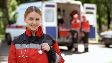 Kamera, arka plan üzerinde bulanık ambulans ekibi içine gülümseyen kadın sağlık görevlisi