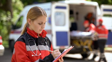 Kadın doktor tıbbi kayıtlar, hasta taşıyan ambulans ekibi tutuyor
