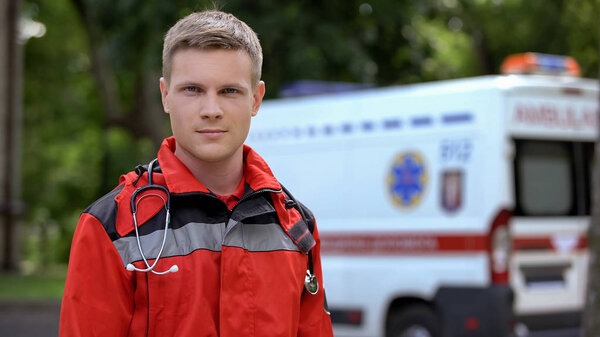 Male paramedic posing for camera, ambulance on background, professionalism