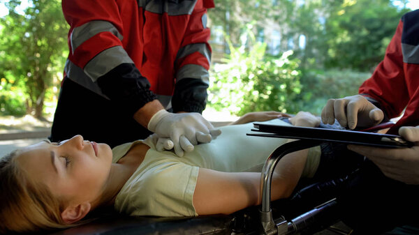 Male paramedic doing indirect heart massage, colleague using tablet for records