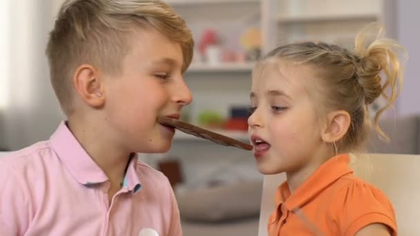 Chico y chica comiendo barra de chocolate, divirtiéndose, bocadillo poco saludable, alto nivel de azúcar — Vídeos de Stock