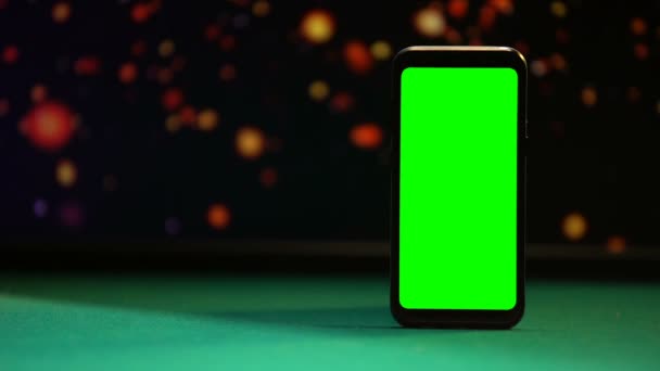 Smartphone com tela verde na mesa de poker, luzes cintilantes no fundo — Vídeo de Stock