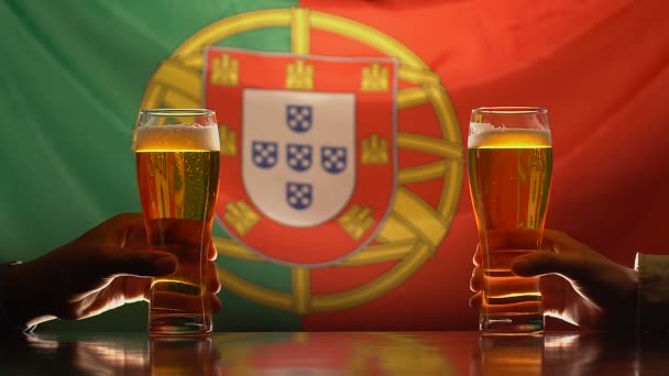 Amigos varones sosteniendo vasos de cerveza, bandera portuguesa en el fondo, celebración — Vídeo de stock