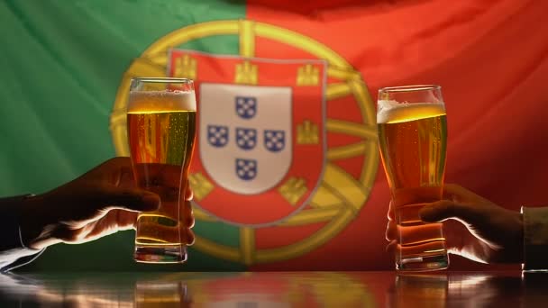 Los partidarios del deporte masculino tintineo vasos de cerveza, bandera portuguesa en segundo plano — Vídeo de stock
