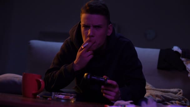 Беспокойный мальчик-подросток курит и играет в компьютерные игры, никотиновая зависимость — стоковое видео