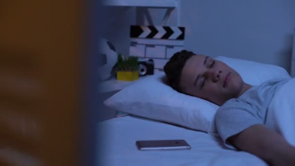 Сонный подросток проверяет время на смартфоне рано утром в выходные, отдыхает — стоковое видео