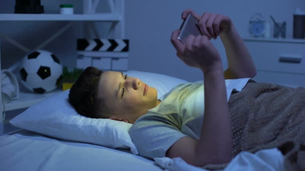 Adolescente desplazarse smartphone, ponerlo en la cama y quedarse dormido, relajación — Vídeo de stock