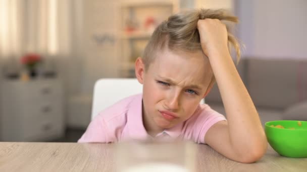 Caprichoso chico masculino mirando tristemente vaso de leche en la mesa de la cocina, comida saludable — Vídeos de Stock