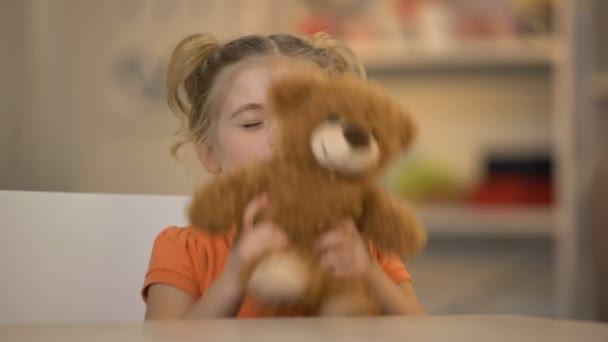 Menina sorridente adorável segurando urso de pelúcia marrom, criança alegre, infância feliz — Vídeo de Stock