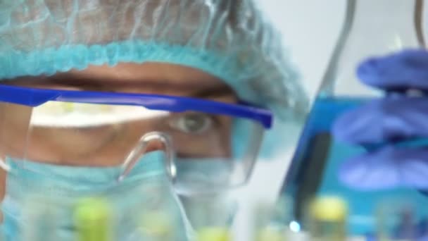 Ученый держит фляжку с голубой жидкостью и трубку с растительной, органической косметикой — стоковое видео