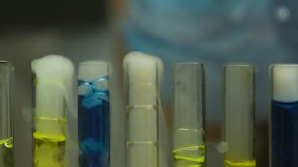 Trabajador de laboratorio goteando líquido en tubos de ensayo en ebullición, monitoreo de reacción química — Vídeos de Stock