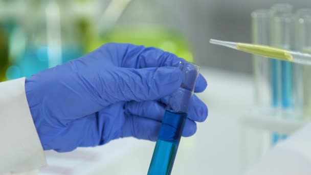 Chercheur de laboratoire ajoutant du liquide vert dans un tube avec une substance bleue, réaction — Video