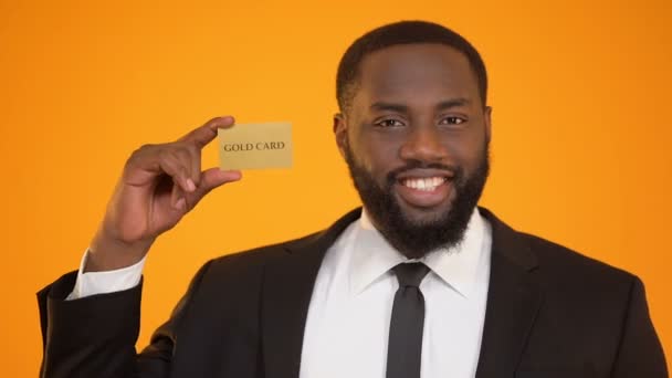 Homem afro-americano auto-confiante em terno formal apresentando publicidade cartão de ouro — Vídeo de Stock