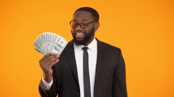 Cheerful afro-american man in formalwear pointing at bunch of dollar cash, coach — Stock Video