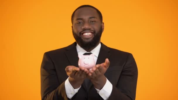 Веселий афроамериканський бізнесмен тримає скарбничку, банківські послуги, депозит — стокове відео