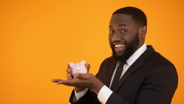Lachende Afro-Amerikaanse man in formalwear schudden spaarpot, bankleningen, activa — Stockvideo