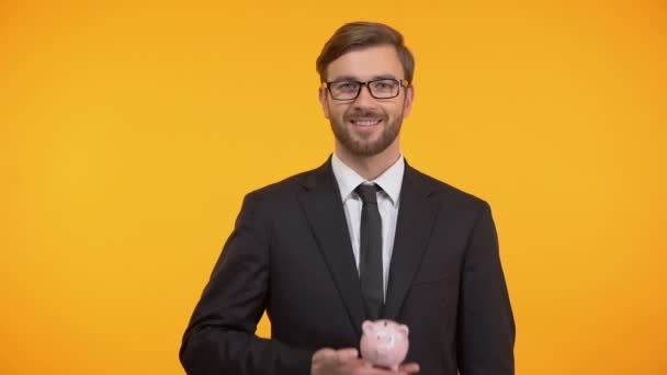 Masculino de terno mostrando porquinho-banco e dólares, fundo de pensão, renda de aposentadoria — Vídeo de Stock