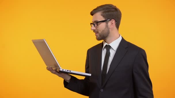 Счастливый фрилансер, держащий ноутбук, подмигивающий и показывающий кучу долларов, успех — стоковое видео