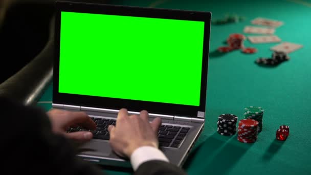 Αρσενικό τζογαδόρος στοιχήματα online πόκερ στο lap-top, κρατώντας το τυχερό ζάρι, πράσινη οθόνη — Αρχείο Βίντεο