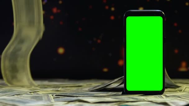 Geld vallen op tafel rond groen scherm smartphone, winst op internet — Stockvideo