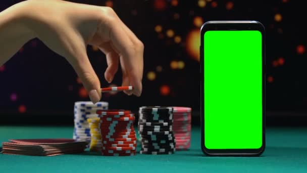 Женщина добавляет жетон в большую кучу, смартфон с зеленым экраном, онлайн казино — стоковое видео
