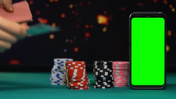 Croupier feminino cartas de negociação perto de pilhas de chips e smartphone tela verde — Vídeo de Stock