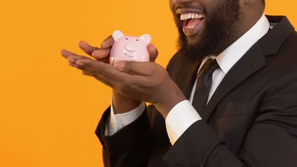 Opgewonden van zwarte man in pak schudden piggy bank, wachten op start-up winst — Stockvideo