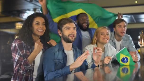 Fãs do esporte extremamente felizes acenando com a bandeira do Brasil em apoio à seleção nacional — Vídeo de Stock