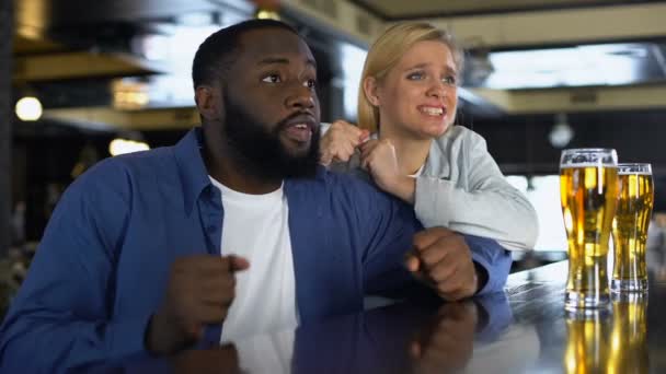 Pareja biracial joven enraizamiento equipo deportivo favorito en el bar, viendo partido en línea — Vídeo de stock