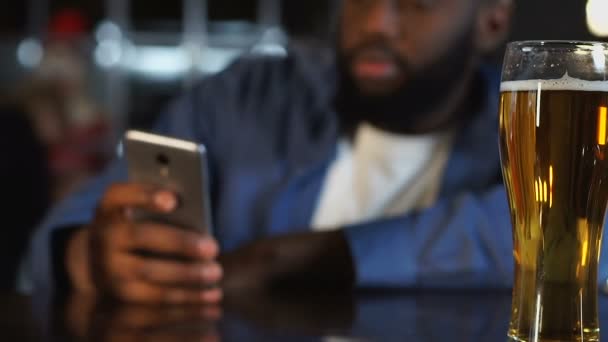 Uomo afroamericano trascorrere del tempo in pub, bere birra e chattare al telefono — Video Stock