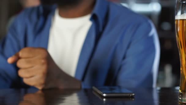 Афро-американец смотрит спортивные соревнования в уютном пивном ресторане, делая ставки — стоковое видео