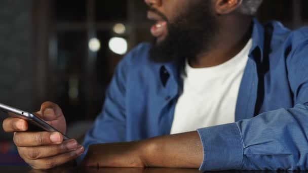Афро-американец общается с посетителями бара, заказывая такси в приложении для мобильных телефонов — стоковое видео