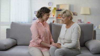 Unhappy mature female and daughter hugging sitting on home sofa, loss breakup