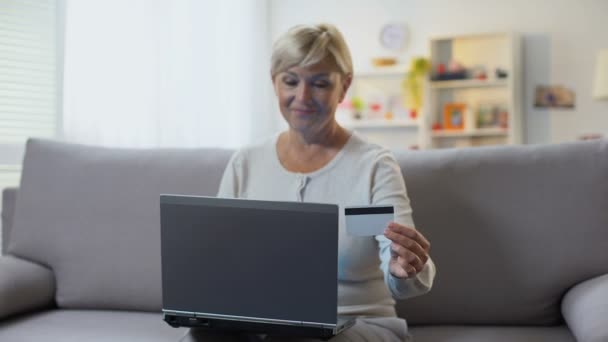 Dojrzały Blondynka kobieta wprowadzanie numer karty kredytowej na laptop siedzi sofa, płatności — Wideo stockowe