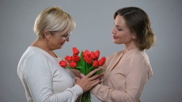 Молода жінка представляє старшу матір з тюльпанами і обіймами, любов'ю і доглядом — стокове відео