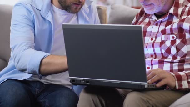 Hijo mostrando a padre adulto cómo hacer videollamada en el ordenador portátil, tecnología moderna — Vídeos de Stock