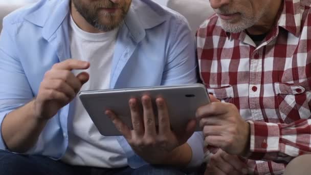 Son teaching his father how to use tablet, happy men smiling for camera, closeup — Stock Video