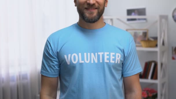 Zelfverzekerd man in t-shirt met vrijwilliger inscriptie glimlachend naar de camera, ondersteuning — Stockvideo