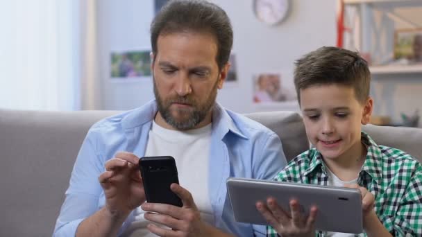 Хлопчик використовує планшет, батько прокручує на смартфон вдома, відсутність зв'язку — стокове відео