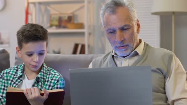 Chłopiec czytanie książki, Dziadek za pomocą laptopa w domu, edukacja w różnym wieku — Wideo stockowe