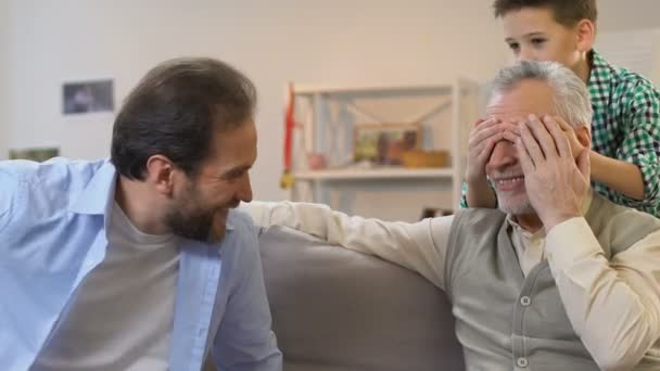 Barnbarn stängning morfar ögon, far ger present ask, födelsedag överraskning, familj — Stockvideo